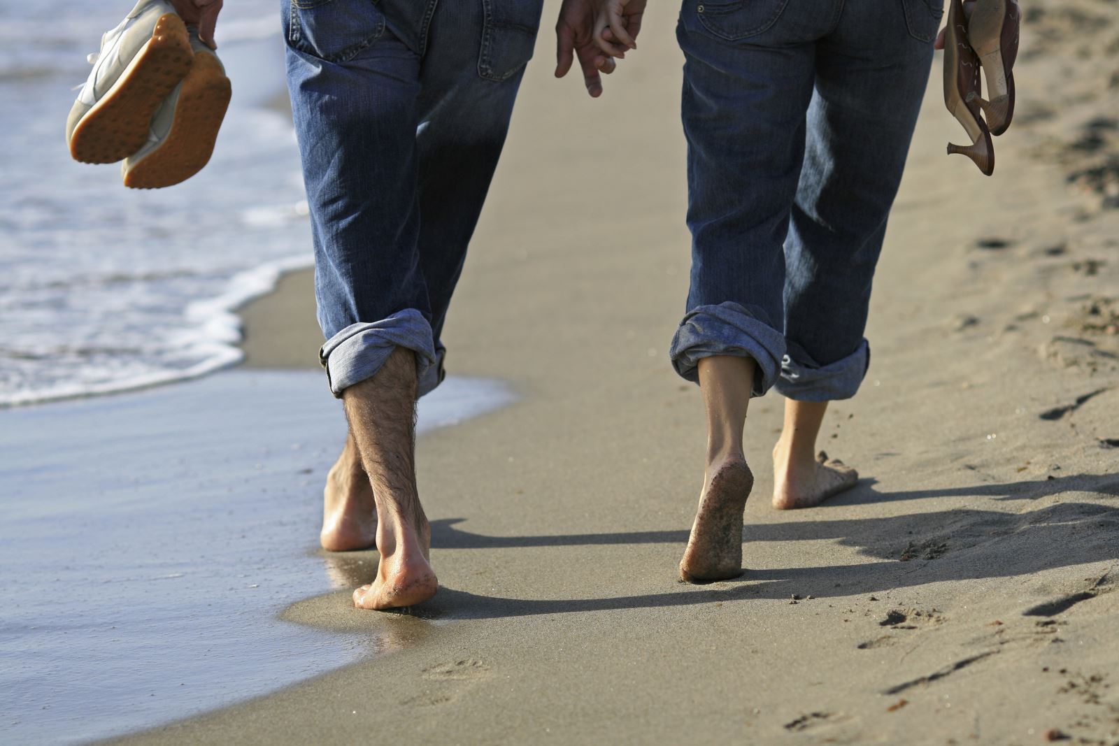 Image of a couple strolling on the beach holding hands