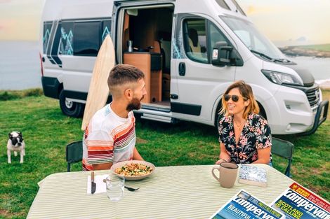 image of a couple sitting outside a campervan with OAL campervan magazines on the table
