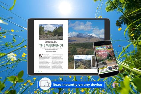 Tablet and smartphone displaying the digital motorhomers magazine with scenic landscape photos, set outdoors among green grass and flowers under a bright blue sky.