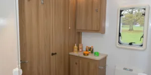 Under-a-hinged-lid-on-top-of-the-cabinet-in-the-corner-is-a-linen-bag-is-suspended-on-four-hooks-87586