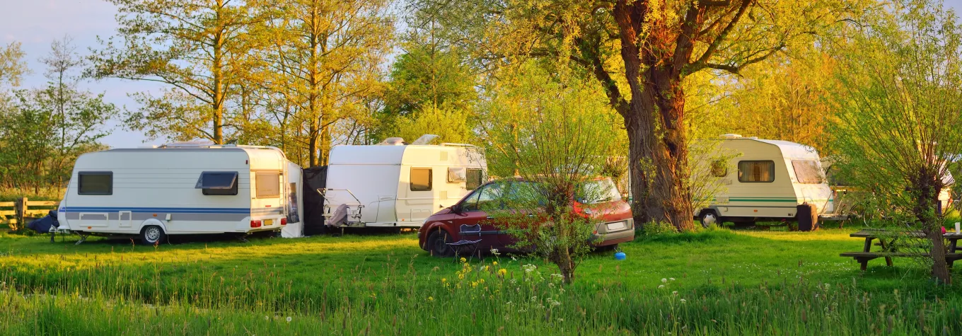 Caravan and a car parked on a green lawn in a camping site. Idyllic spring landscape. Holland. RV, transportation, road trip, vacations, ecotourism, travel, lifestyle, recreation