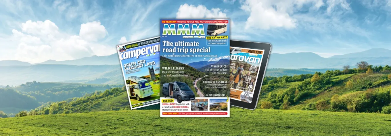 motorhome, campervan and caravan magazines stacked over a scenic road trip landscape.