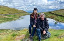 Paul Merton and Suki Webster sitting on a hillside nearby a rural motorhome pitch.