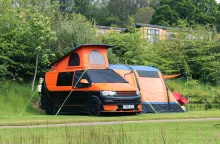 image of an orange and black campervan set up on a campsite