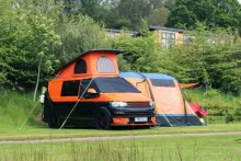 image of an orange campervan pitched up on a field