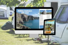A desktop monitor and tablet displaying a digital issue of Caravan magazine, set outdoors on a campsite with caravans, trees, and camping equipment in the background.