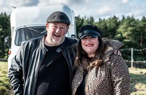 Johnny Vegas standing outside a vintage motorhome at a glamping site