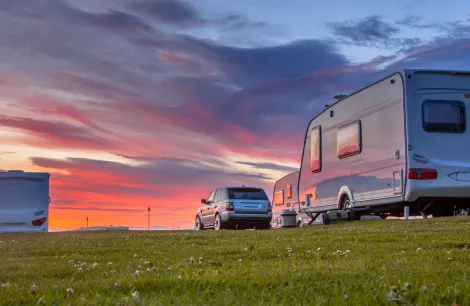 caravans and cars parked on a grassy campsite under a beautiful sunset