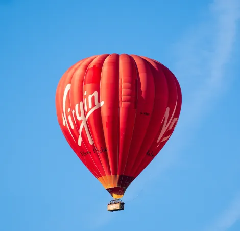 Red Virgin Hot air Balloon Flights in the sky with passengers in the basket
