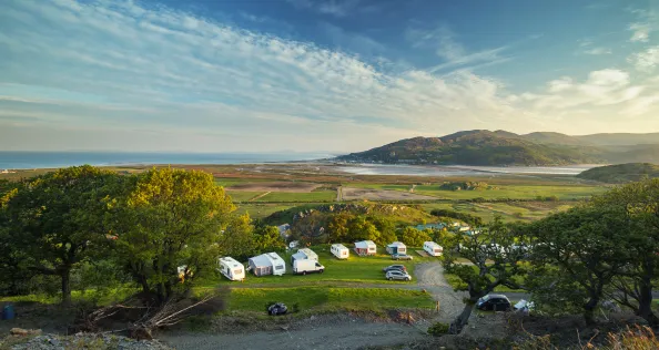 Elevated view over coastal campsite on hill slope with scenic views over Barmouth estuary at sunrise