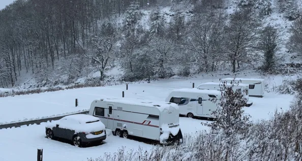 A caravan pitched in a campsite facing a snowy hillside view